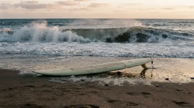 Planche de surf dans le sable devant une vague qui déferle