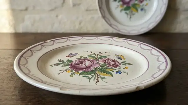 Assiette de faïence blanche à grosse rose de manganèse, œillet et papillons, posée sur du chêne