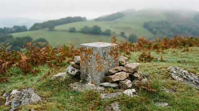 Borne de granit couverte de lichen et cairn de pierres au sommet, collines dans la brume