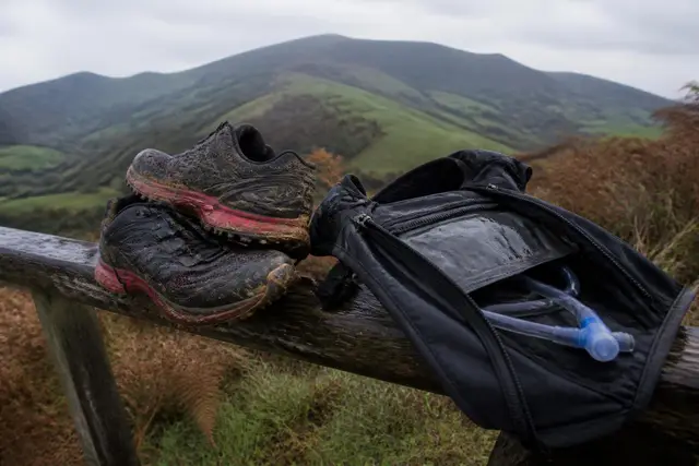 Chaussures de trail crottées et sac d'hydratation posés sur une barrière de pâturage