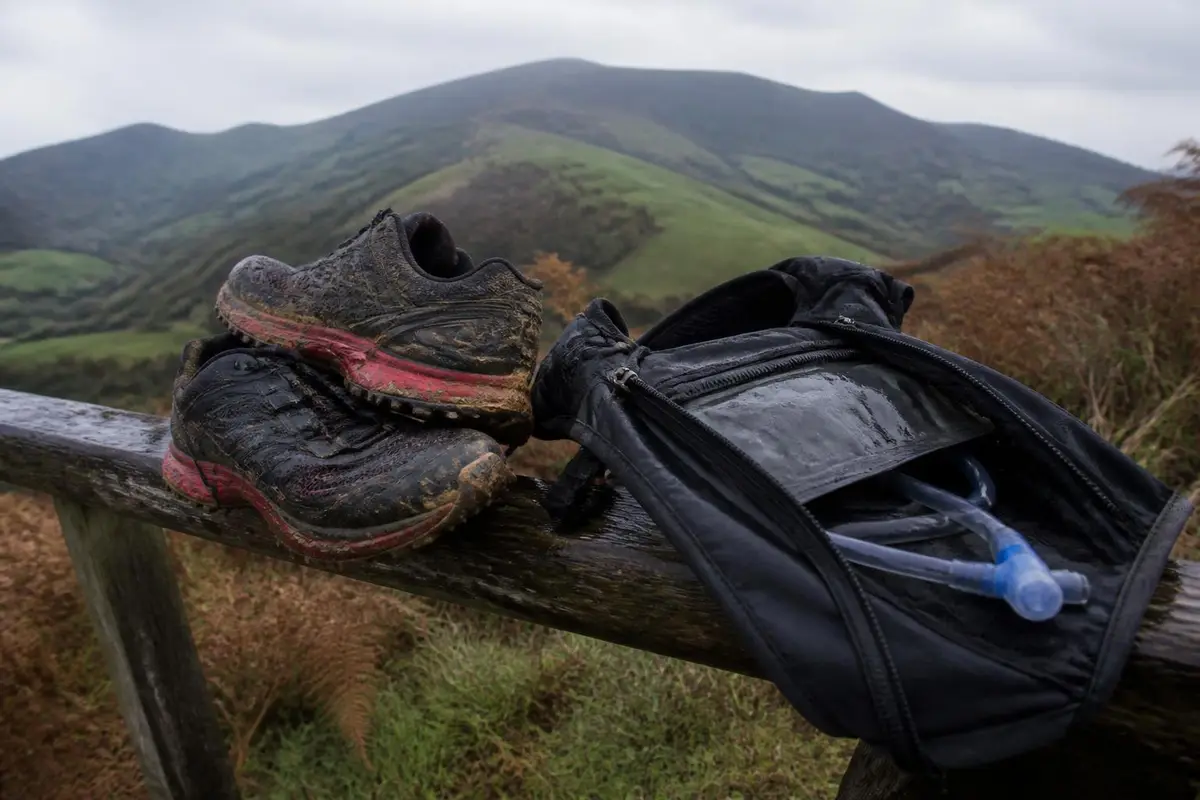 Chaussures de trail crottées et sac d'hydratation posés sur une barrière de pâturage