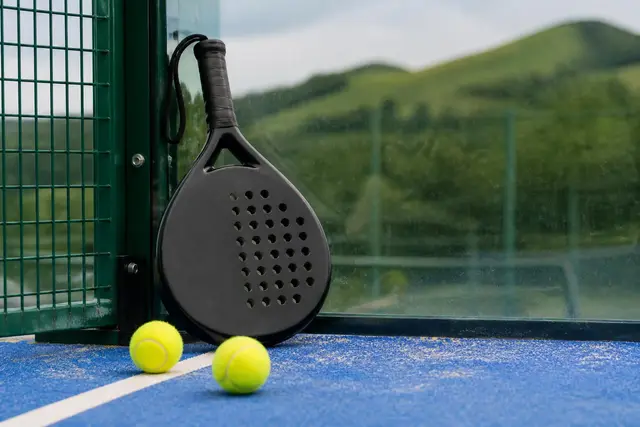 Raquette de padel et balles posées contre la vitre d'une piste extérieure